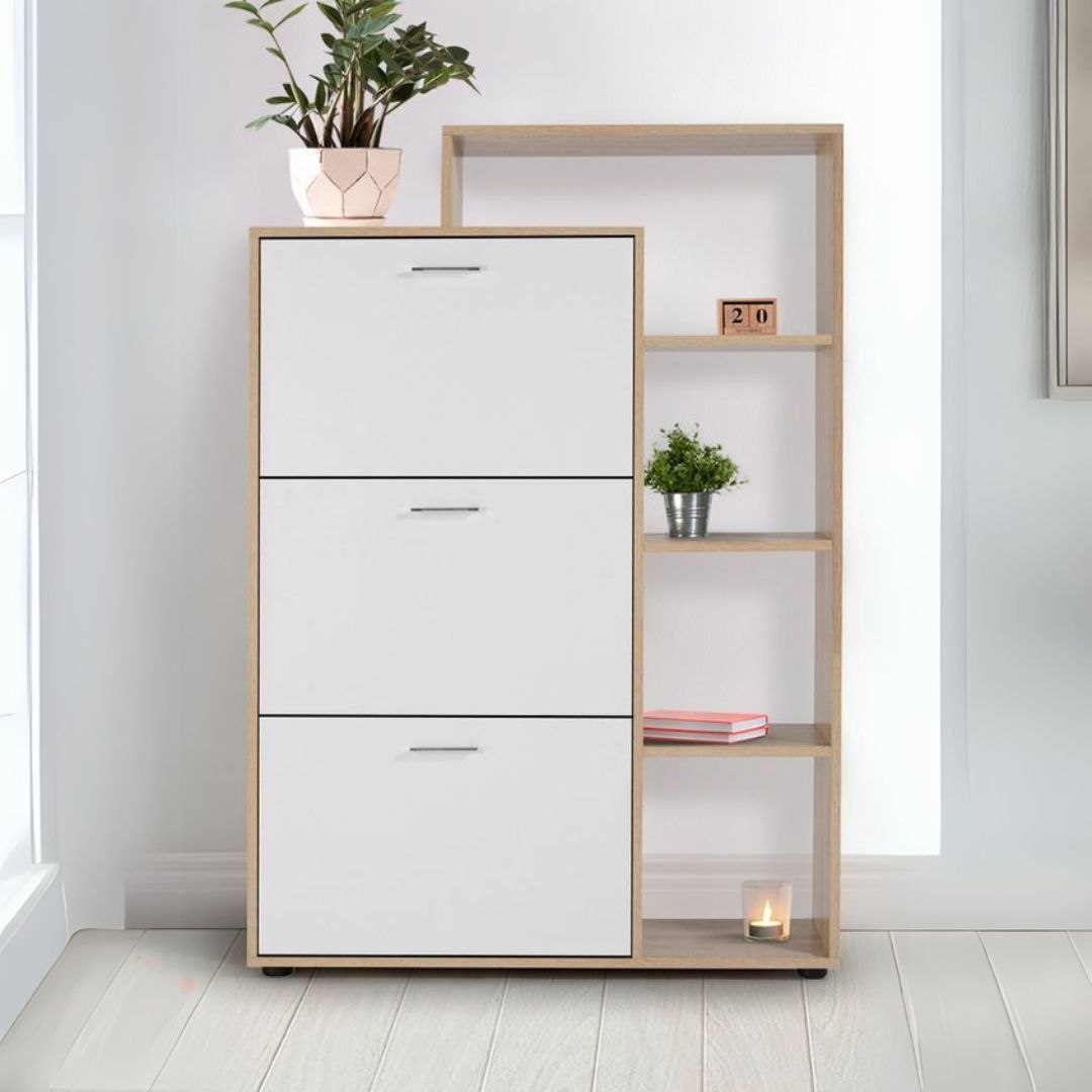 A modern three-drawer storage cabinet with a light wood frame and open shelving on the right side, styled with a potted plant, small green plant, books, and a candle in a bright room.