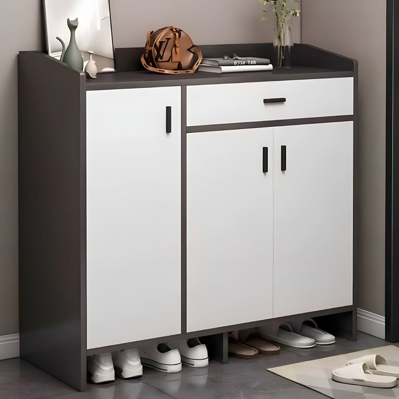 A modern 3-door entryway shoe cabinet with a dark gray top and frame, white doors, and black handles. The cabinet is styled in a home entryway with decorative items on top and shoes stored underneath.