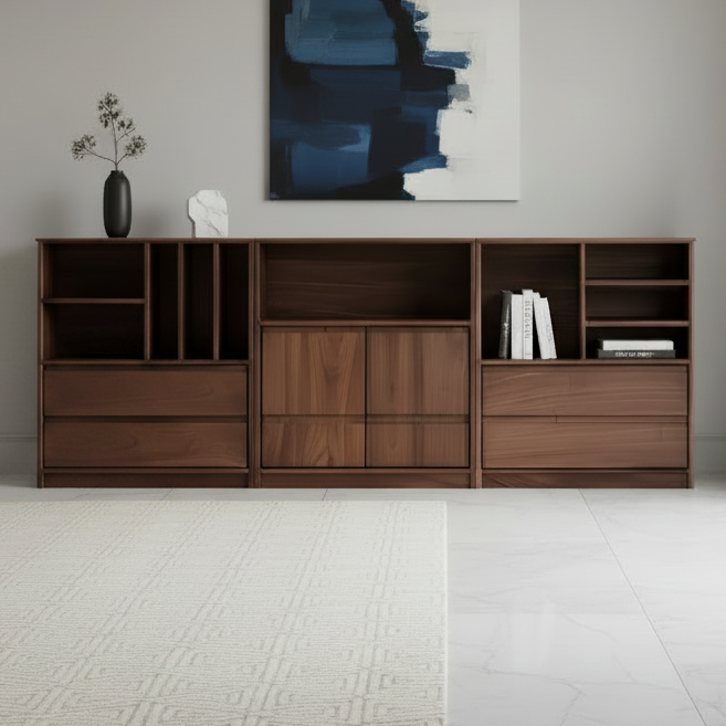 A modern wooden sideboard or console cabinet in a warm medium brown finish, styled in a minimalist living room setting with a beige sofa, a table lamp, a small potted plant, and a blue-gray abstract painting on the wall.