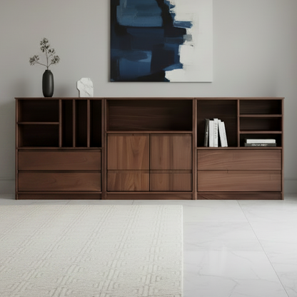 A modern wooden sideboard or console cabinet in a warm medium brown finish, styled in a minimalist living room setting with a beige sofa, a table lamp, a small potted plant, and a blue-gray abstract painting on the wall.