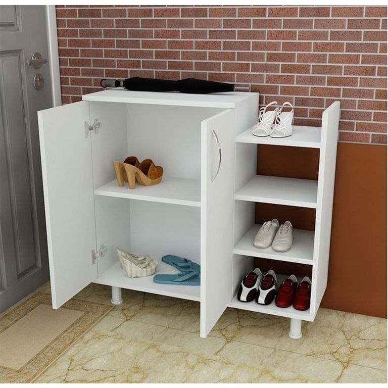 A white entryway shoe cabinet with two doors open, showing shelves and open side compartments filled with shoes. The cabinet stands on a tiled floor against a brick wall and door background.
