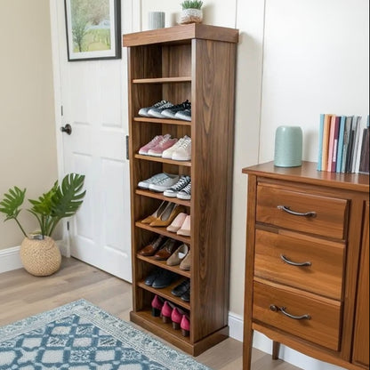 A tall wooden shoe rack with five open shelves, filled with various shoes, standing in a bright entryway next to a white door and a patterned rug.