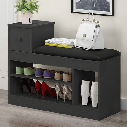 A dark gray entryway bench with a black cushioned seat, featuring a small side drawer, open shoe storage shelves, and display pockets. The bench is styled with a white handbag, books, a small potted plant, and several pairs of shoes, set in a home entryway environment.