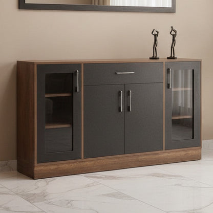 A modern sideboard cabinet with a dark charcoal black center and warm brown wood grain sides and top, featuring two glass-front cabinets with dark handles and a single drawer with a silver handle. It is styled in a room setting with a textured gray wall, a rectangular mirror, and a potted plant.