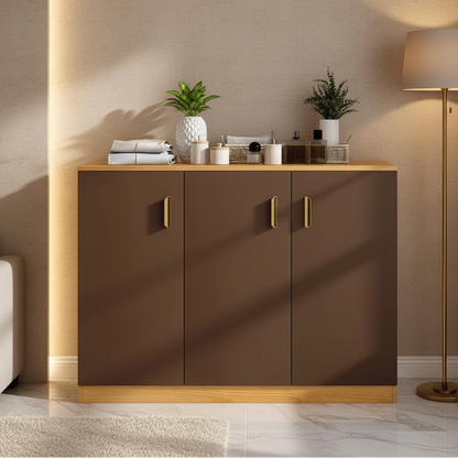 A modern three-door cabinet in a warm brown finish with light wood trim and gold handles, styled in a minimalist room with a floor lamp, plants, and decorative items.