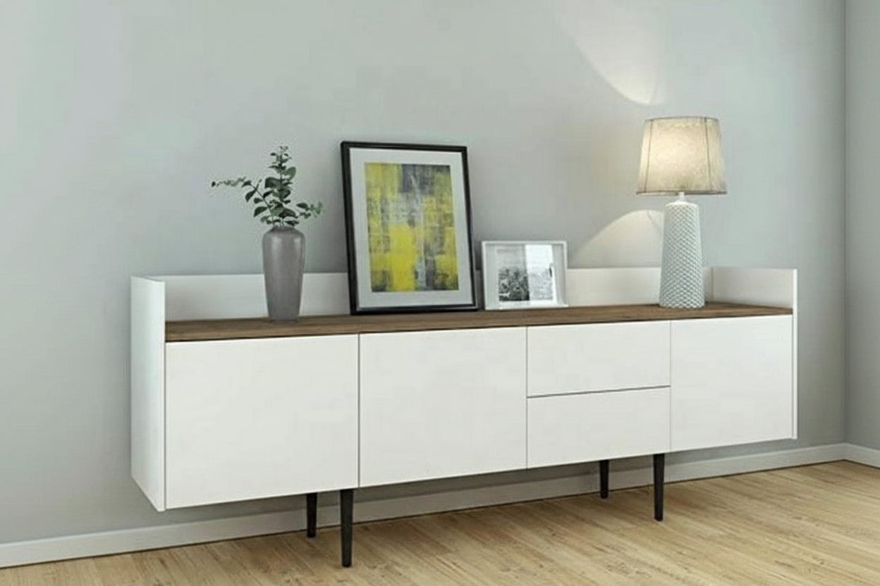 A modern white sideboard cabinet with a light brown wood-look top, black tapered legs, and decorative items including a vase, framed art, and a table lamp, set against a light gray wall and light wood floor.